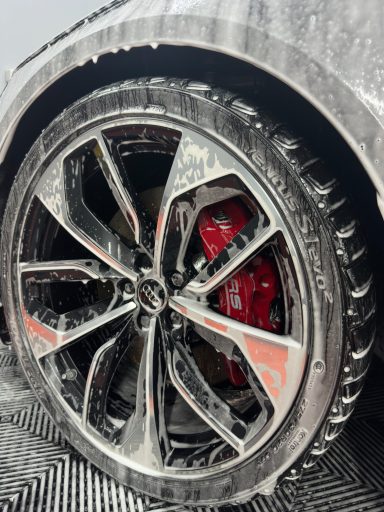 Jante de voiture avec un nettoyage, mettant en valeur des freins rouges et un effet mousse.
