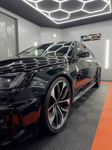 Voiture noire brillante, avec des jantes sportives, stationnée dans un garage moderne.
